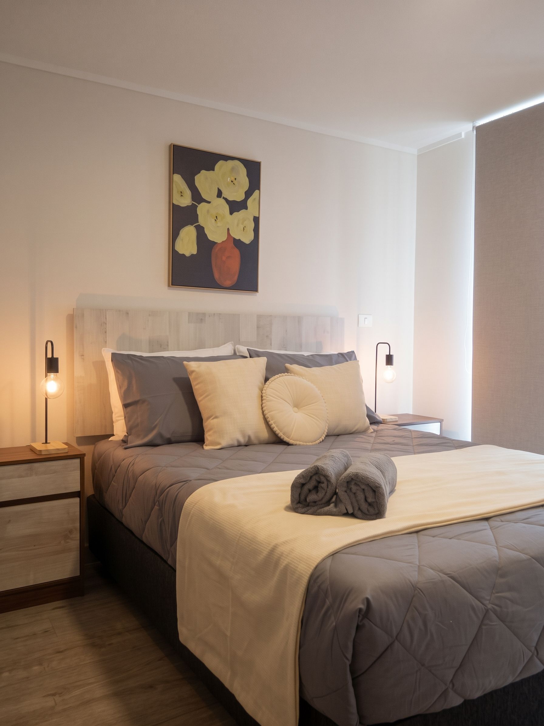 Une chambre à coucher moderne, comprenant un lit, des tables de chevet, une tête de lit et une œuvre d’art accrochée au mur.
