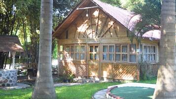 Uma casa de madeira com telhado inclinado, cercada por um gramado bem cuidado e árvores.