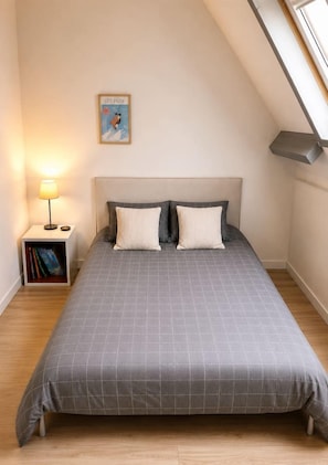 Et soveværelse med en seng, et natbord, en lampe og et billede på væggen.