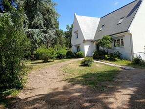 Una casa con techo inclinado, un jardín delantero con camino de grava y vegetación circundante.