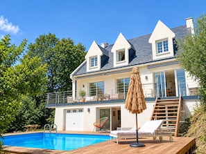 Una casa de dos pisos con piscina, un balcón con mobiliario exterior y una escalera que lleva al piso superior.