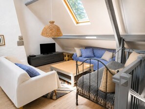 En storbådenlig opholdsstue med højt til loftet, ovenlys, sofa, sofabord, fjernsyn og en fletstol.