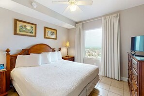 Une chambre d’hôtel avec un grand lit, une télévision, une fenêtre avec des rideaux et des œuvres d’art accrochées au mur.