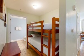 A bunk bed room with a wooden bench, a door leading to a bathroom, and a ceiling light. - 🌊 Tidewater 2110 🏖️ Beach Front | 🌅 Private Balcony | 🏊 Pools 🏖️ (Panama City Beach)