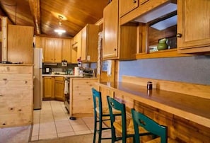A wooden kitchen with a bar area, wooden cabinets, and a tiled floor. - Milner Pass Cabin/ Cozy Mountain retreat in South Fork, CO (Alpine)