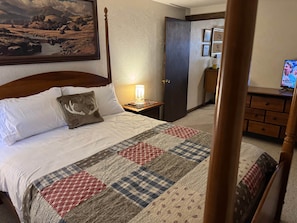 A hotel room with a bed, a nightstand with a lamp, a dresser, and a painting on the wall. - Milner Pass Cabin/ Cozy Mountain retreat in South Fork, CO (Alpine)