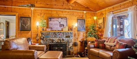 A log cabin interior with a fireplace, leather furniture, and wooden walls.