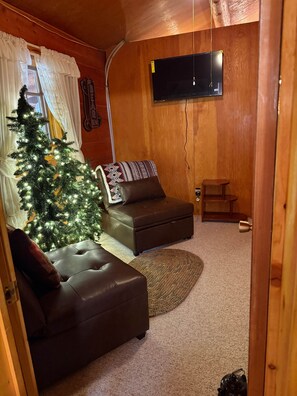 A cozy living room with a leather sofa, a small ottoman, a Christmas tree, and a flat-screen TV mounted on the wall. - Milner Pass Cabin/ Cozy Mountain retreat in South Fork, CO (Alpine)