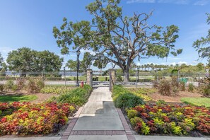 A pathway leading to a gated entrance with a large tree and a lamp post. - Los Olas 3 🌊🚀 Rooftop Terrace for Ocean Views + Rocket Launches (Ormond Beach)