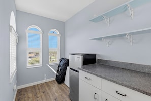 A kitchen with a refrigerator, a countertop, and two windows with blinds. - Los Olas 3 🌊🚀 Rooftop Terrace for Ocean Views + Rocket Launches (Ormond Beach)