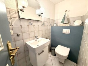 A bathroom with a white sink, a toilet, a mirror with wall-mounted lights, and a small decorative sailboat on the wall. - House 94 - Apt. Ground Floor (Oldsum)