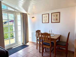 A dining area with a table and chairs, a radiator, and a window with curtains. - House 94 - Apt. Ground Floor (Oldsum)