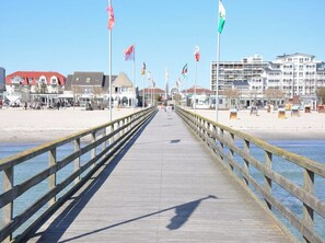 A pier extending into the water with a wooden railing, flags, and buildings in the background. - Holiday Apartment With 1 Bedroom (Grossenbrode)