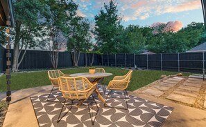 Une terrasse avec une table et des chaises, entourée d’une clôture en bois et d’arbres.