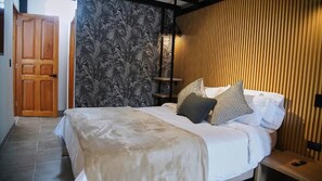 A bedroom with a bed, pillows, a nightstand, a wooden wall, and a door.