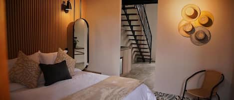 Un dormitorio con cama, espejo, un perchero de pared, una silla y una escalera que lleva a otra habitación.