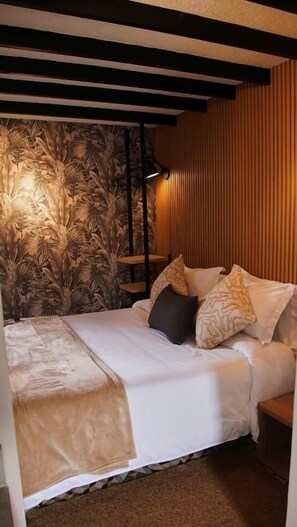 A bedroom with a bed, pillows, a bedside table, and a wall with a floral wallpaper pattern.