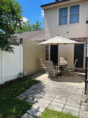 Eine Terrasse mit Tisch und Stühlen, ein weißer Zaun und ein Haus mit Backsteinfundament.