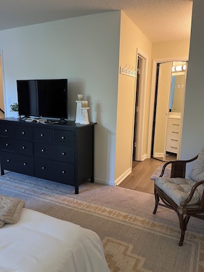 Ein Schlafzimmer mit Bett, Kommode, Fernseher, Stuhl und Spiegel.