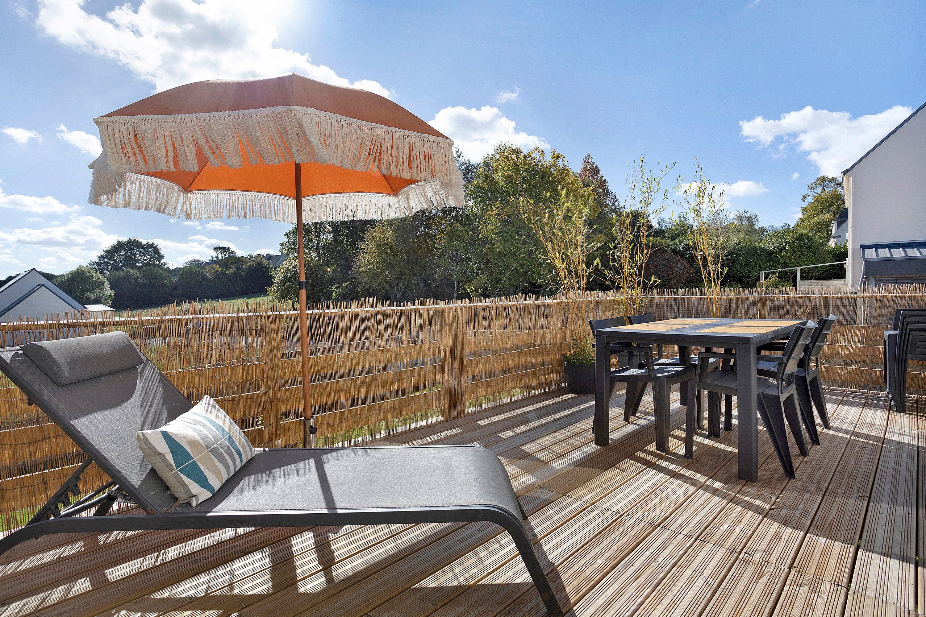 Un patio esterno con tavolo e sedie, una poltrona relax e un ombrellone decorativo.