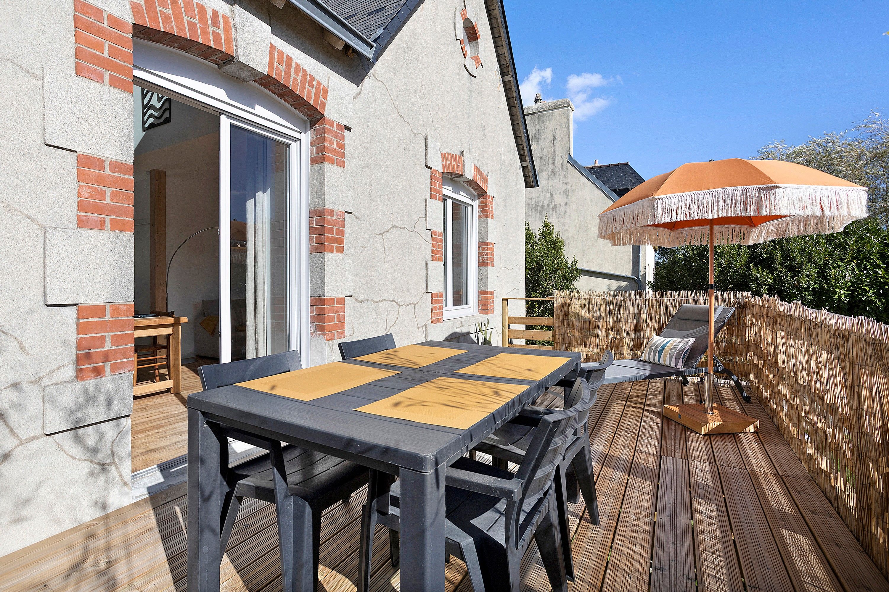 Une terrasse extérieure avec une table et des chaises, une plateforme en bois et un espace salon couvert avec un parasol.