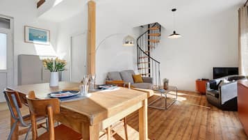 Moderni olohuone, jossa on puinen ruokapöytä, sohva, televisio ja kierreportaat.