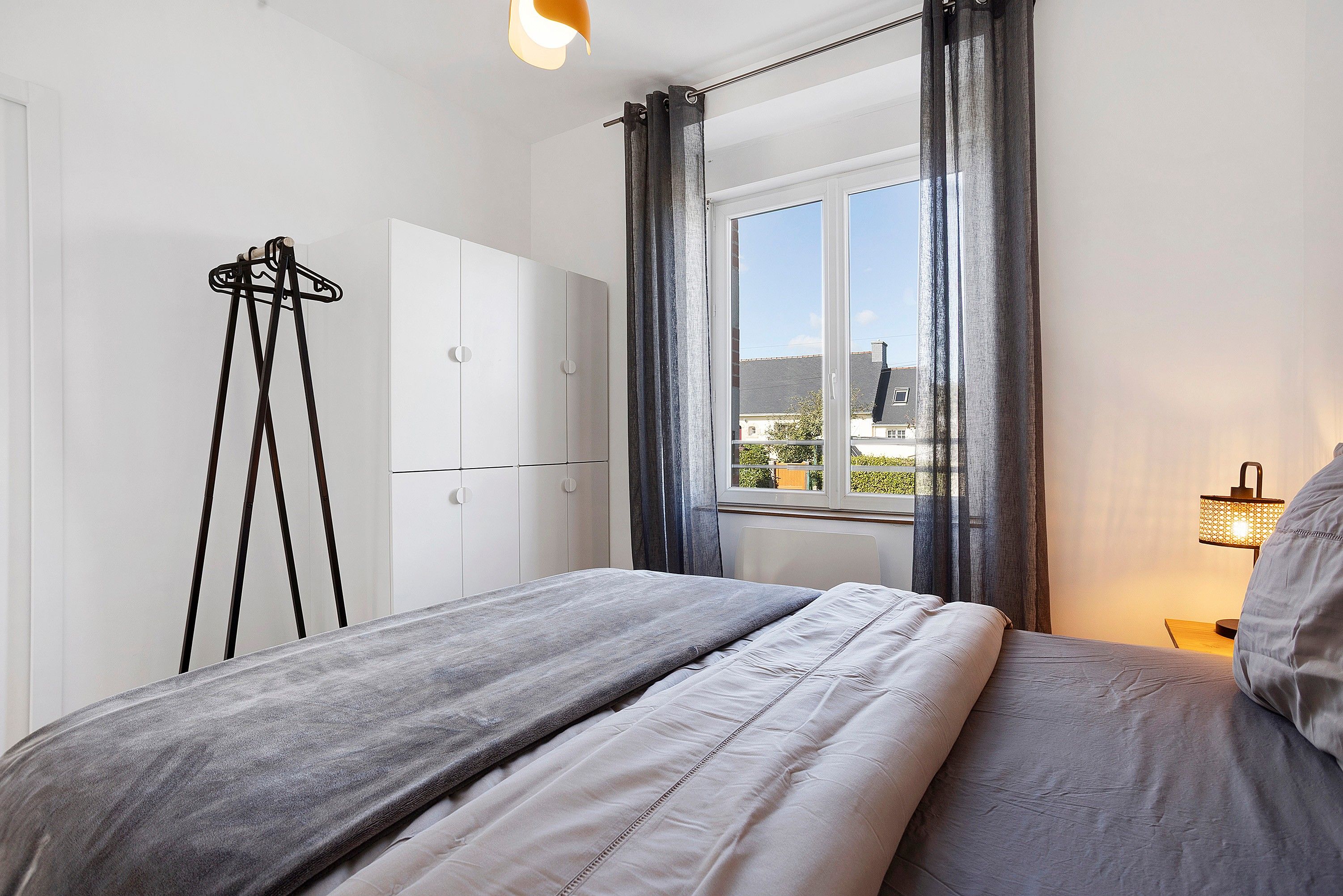 Una camera da letto con un letto, un armadio, un attaccapanni e una finestra con tende.