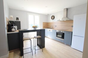 A modern kitchen with a central island, bar stools, a built-in oven, and a stainless steel range hood. - 200 meters from the beach, with access to a heated pool and a game room—ideal for families (Port-Bail-sur-Mer)