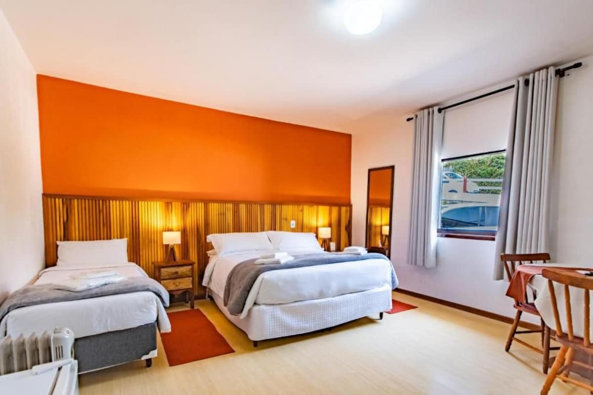 Quarto de hotel com uma cama grande, duas mesas de cabeceira, uma cadeira e uma janela com cortinas.