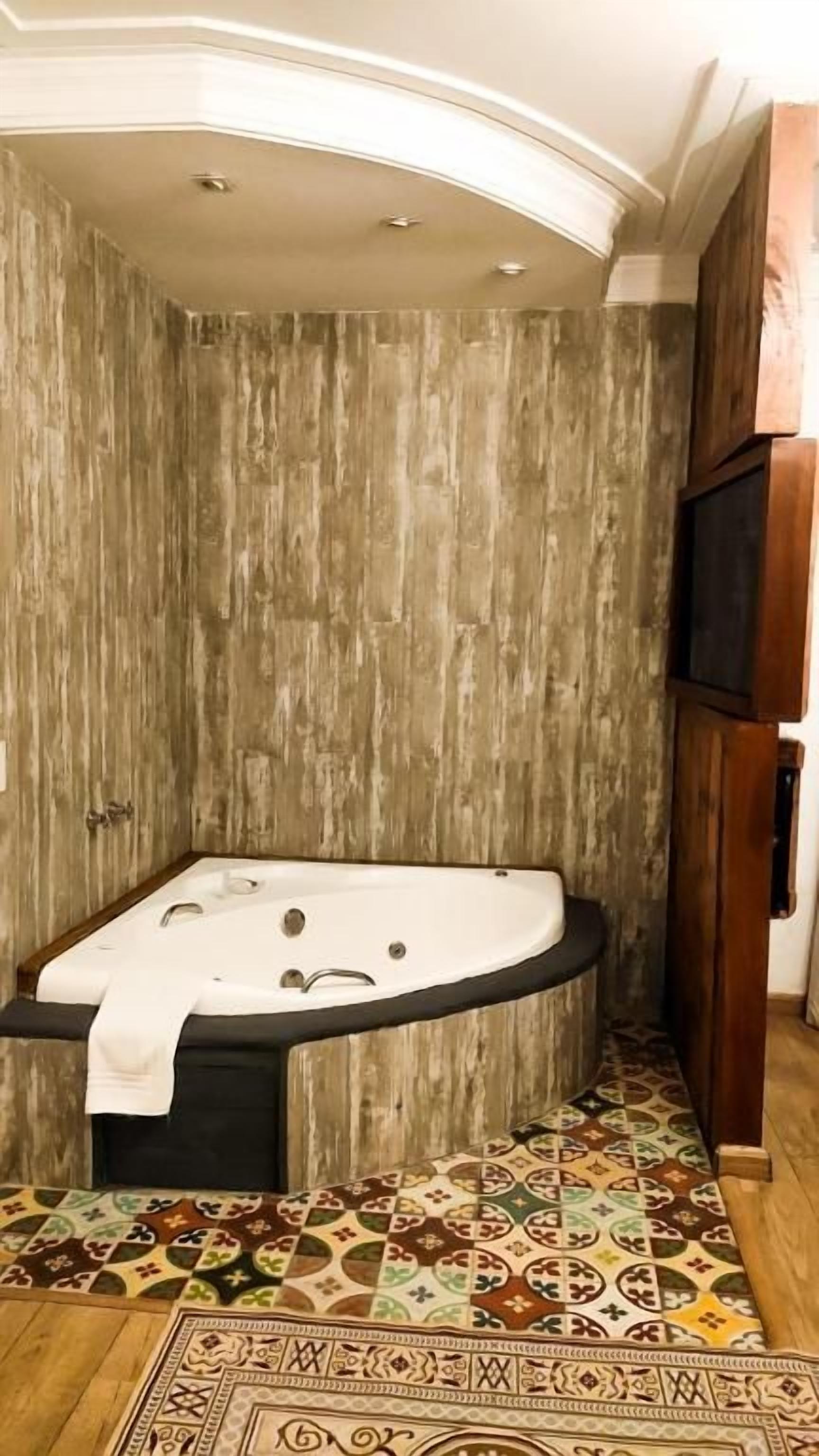 Ein Zimmer mit einer großen, freistehenden Badewanne, einem gemusterten Teppich und einer Holzwand.
