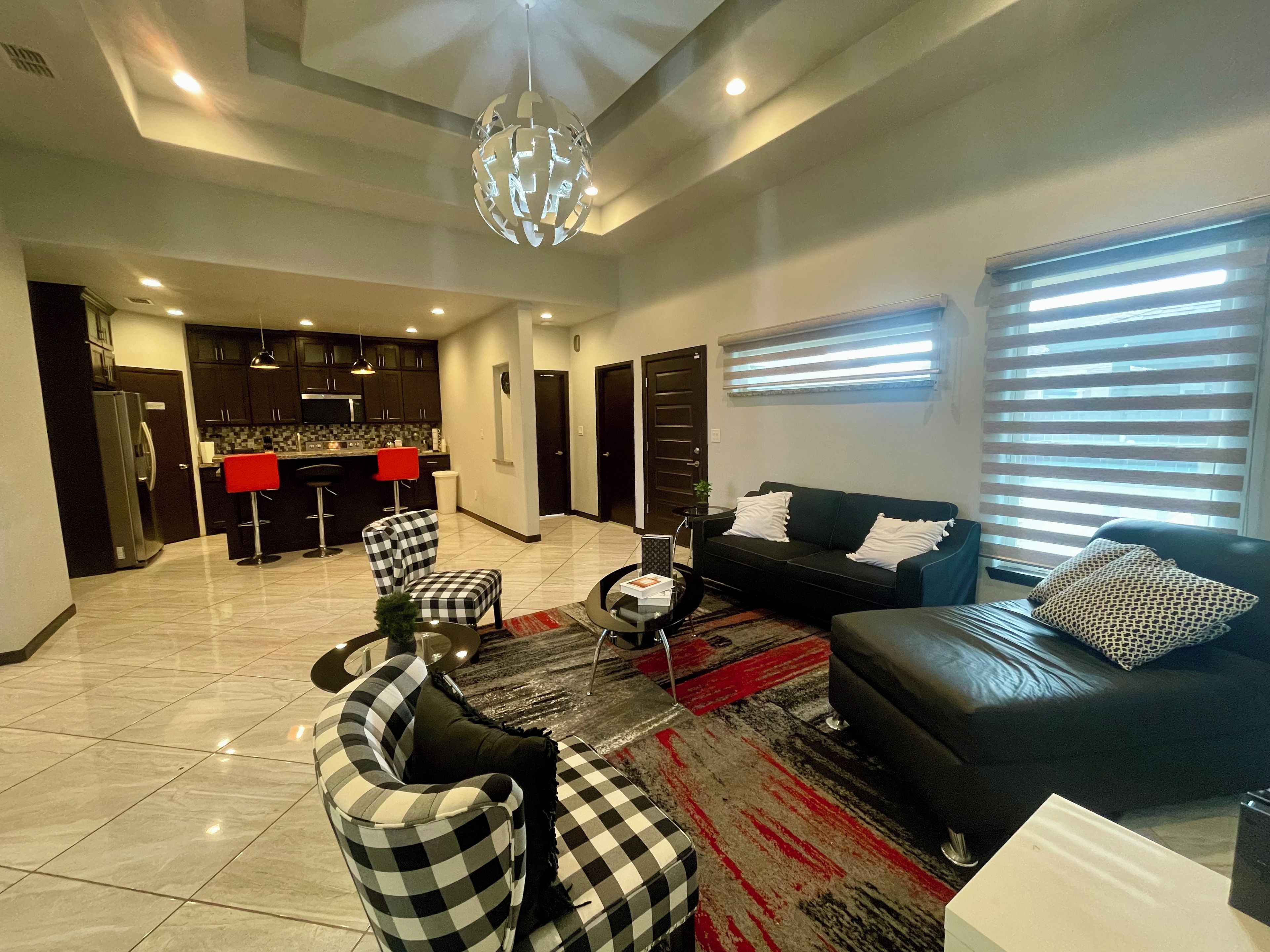 A modern living room with a black sofa, checkered chairs, a coffee table, and a kitchen in the background.