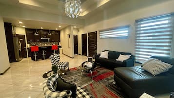 A modern living room with a black sofa, checkered chairs, a coffee table, and a kitchen in the background.