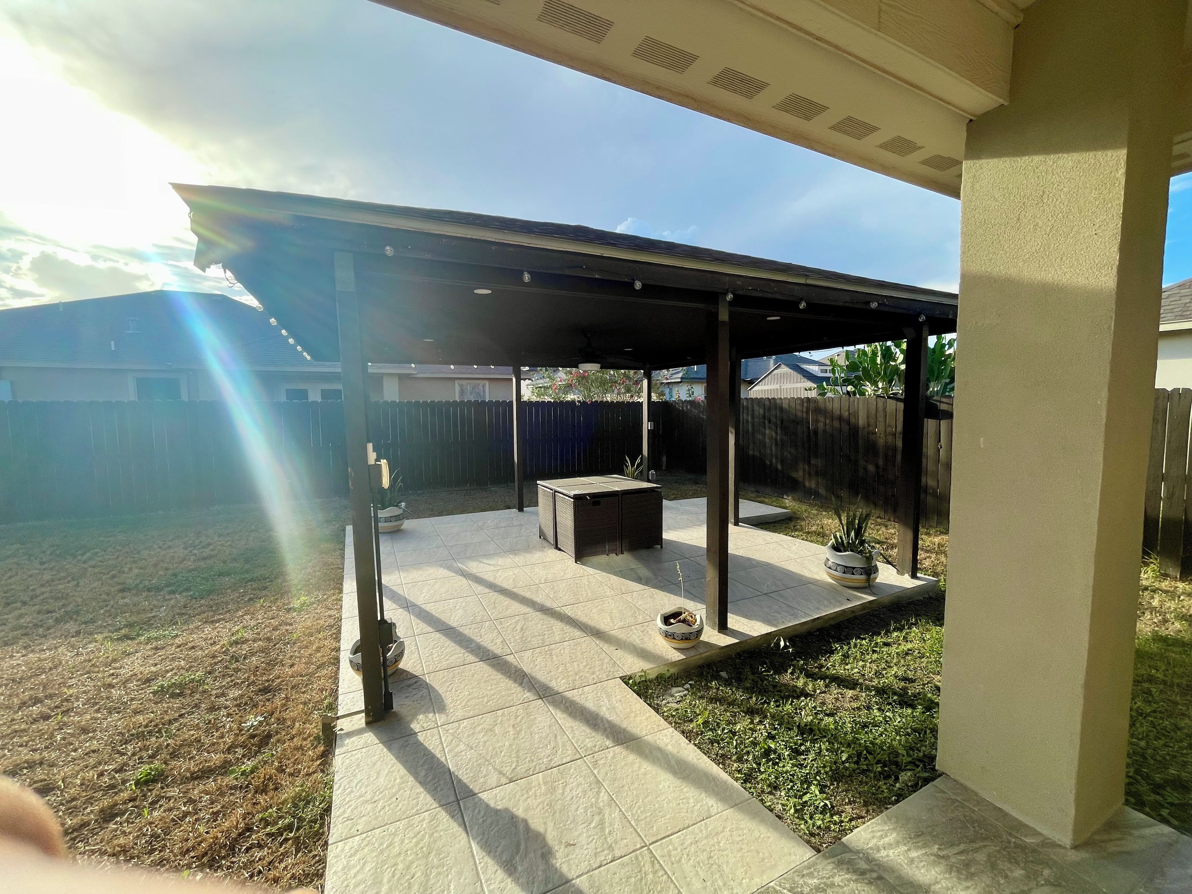 A covered patio area with a tiled floor, a barbecue grill, and a potted plant.
