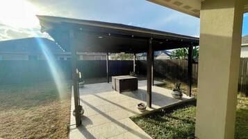 A covered patio area with a tiled floor, a barbecue grill, and a potted plant.