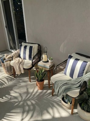 Ein sonniger Außenbereich mit Sitzgelegenheiten für zwei Personen, einem kleinen Tisch und Topfpflanzen.