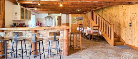 Una cocina rústica con barra de madera, taburetes y una escalera que lleva a un comedor.