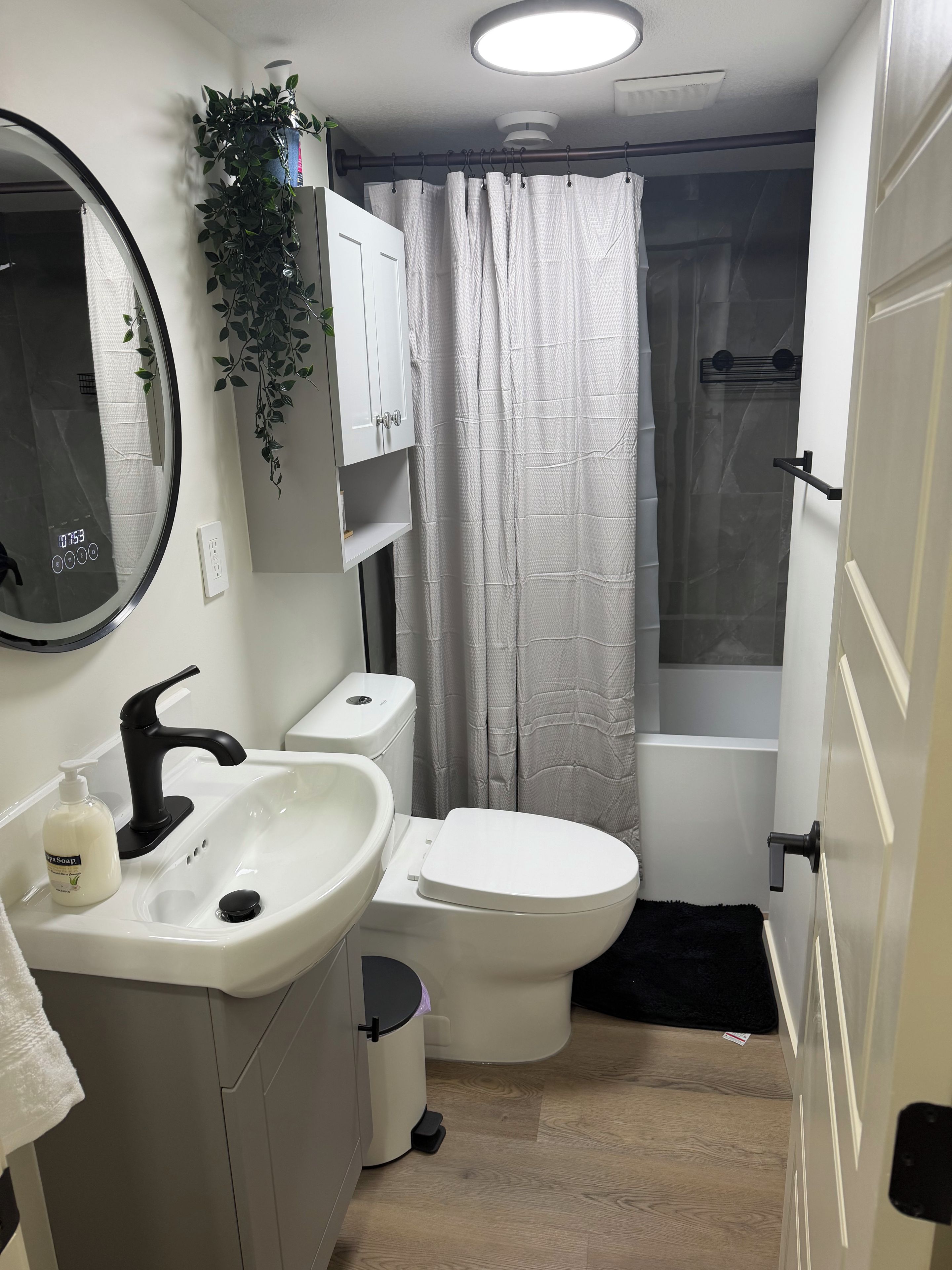 A bathroom with a white sink, black faucet, toilet, and a shower curtain.