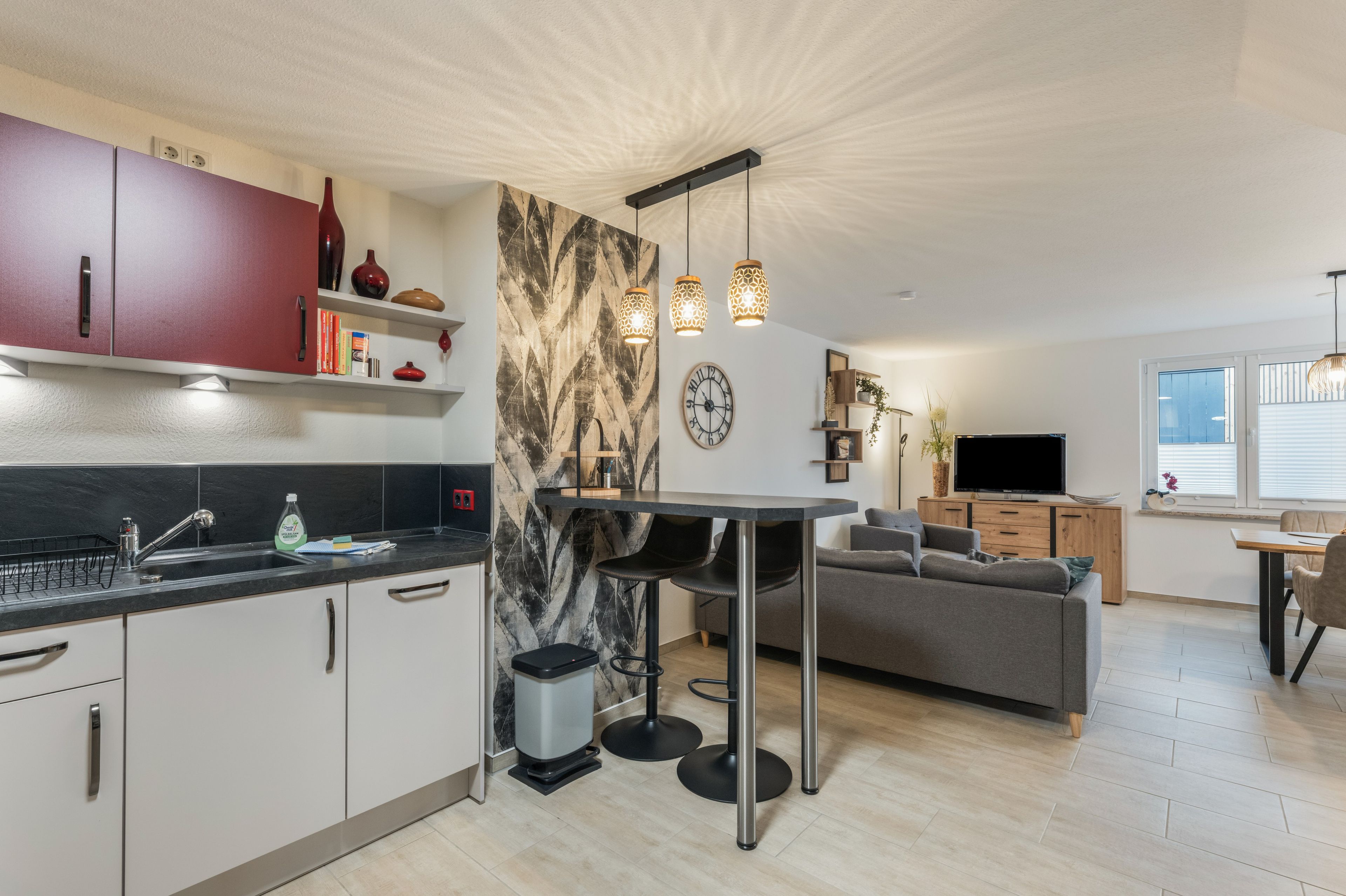 A modern kitchen with white cabinets, a black countertop, and a dining area with a grey sofa and a table.