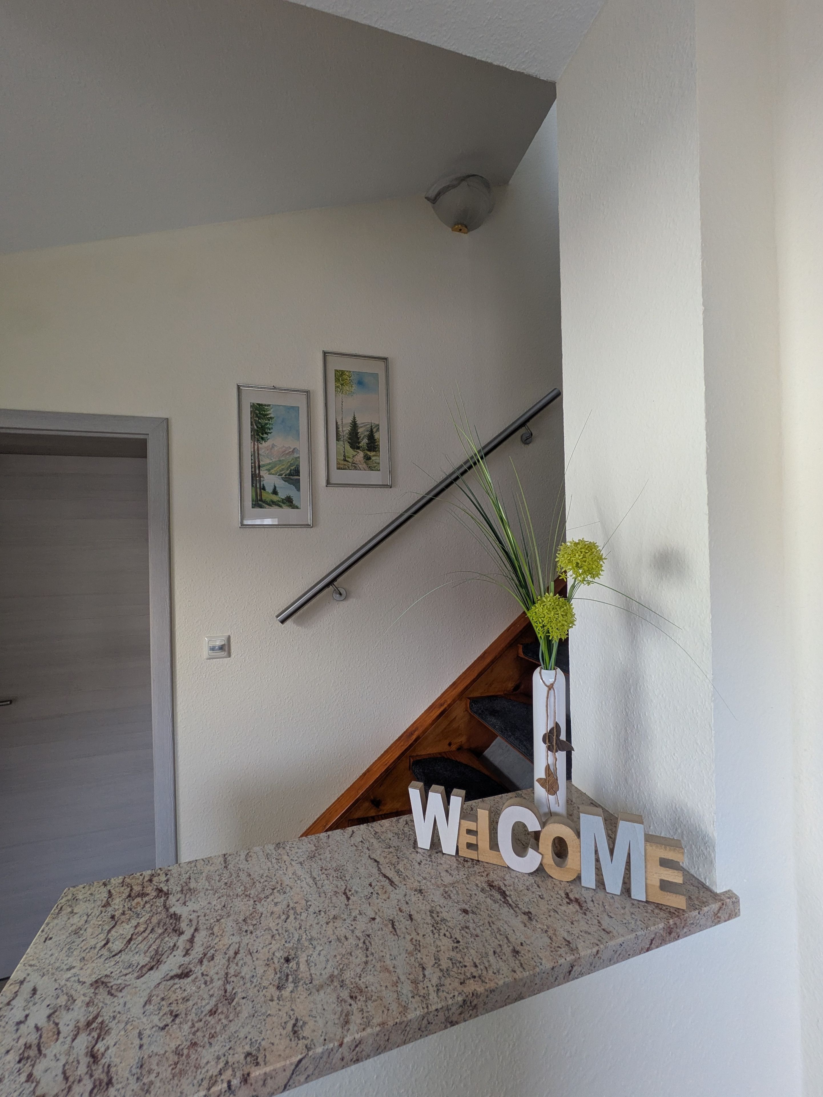 A staircase with a welcome sign, a door, and two framed pictures on the wall.