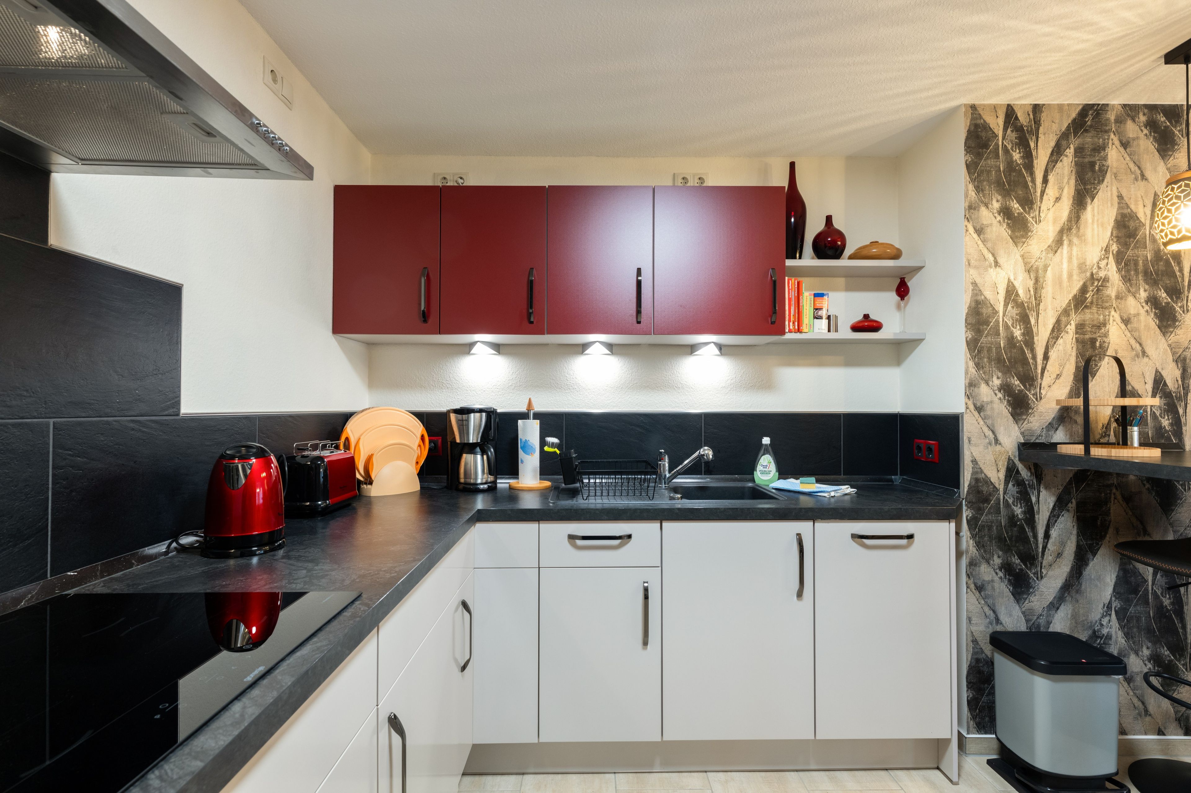 A modern kitchen with white cabinets, a black countertop, and red upper cabinets.