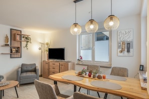 Una sala moderna con un sofá gris, una mesa de comedor de madera y lámparas colgantes.