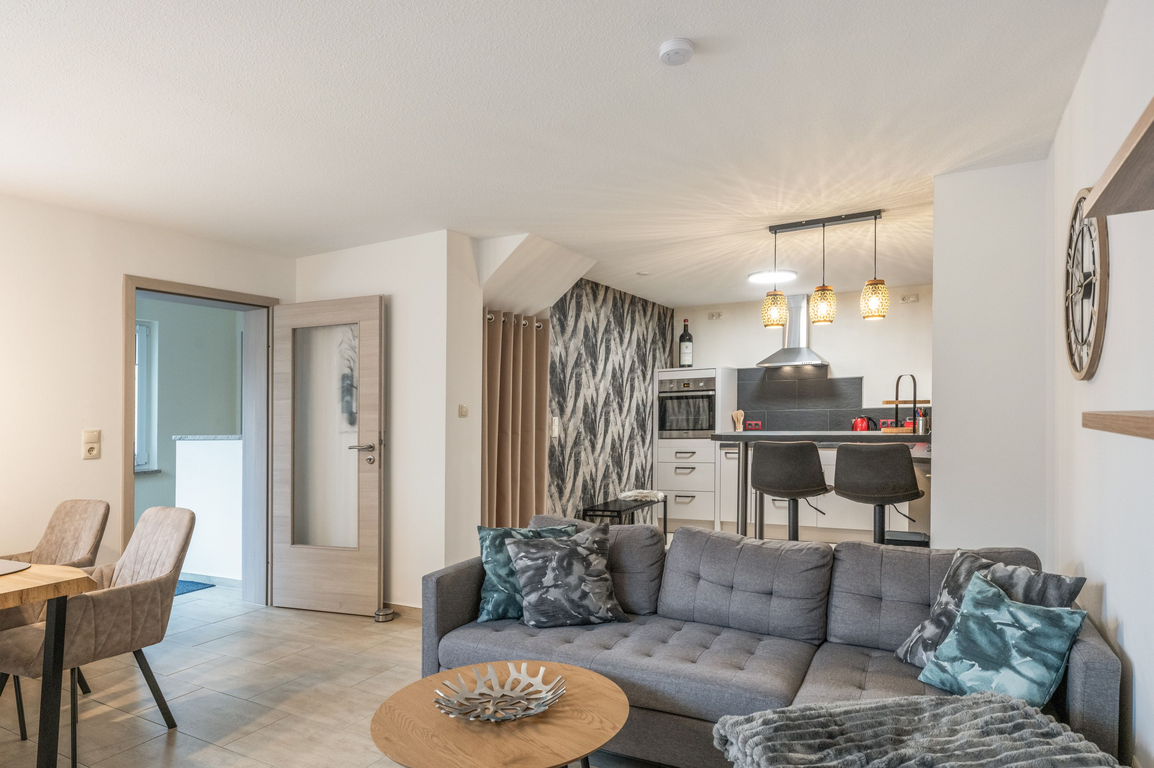 Ein modernes Wohnzimmer mit einem grauen Sofa, einem Holztisch und einem Essbereich mit einem Holztisch und Stühlen.