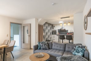 Una sala de estar moderna con un sofá gris, una mesa de centro de madera y una zona de comedor con mesa y sillas de madera.