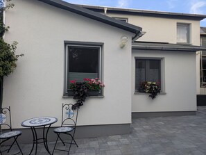 A building with a white exterior, two windows with flower boxes, and a patio area with two chairs and a table. - Holiday home 'Fewo Zum Schlosspark' with Wi-Fi (Ilmenau)