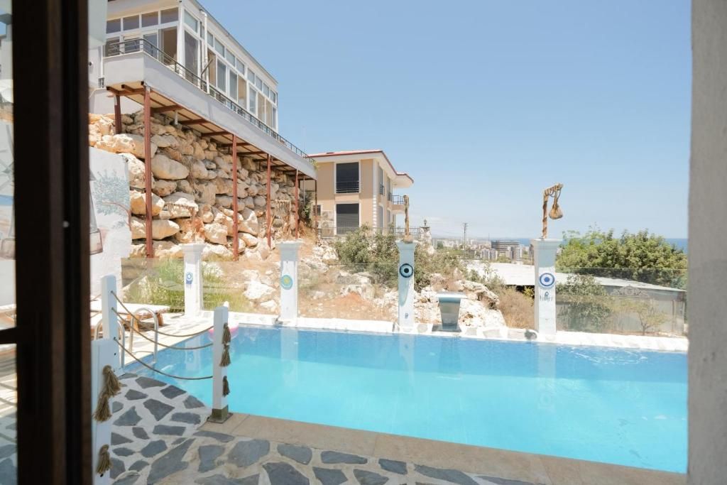 A swimming pool with a stone border, a view of a building with a balcony, and a clear sky.