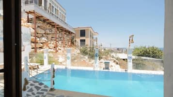A swimming pool with a stone border, a view of a building with a balcony, and a clear sky.