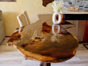 Mesa de jantar com design único na madeira, um vaso com flores secas e uma cesta trançada na bancada.