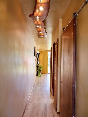 A hallway with wooden doors, a plant, and a ceiling light fixture. - Cozy 1-bedroom condo in charming Paia with AC in the bedroom. (Paia)