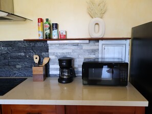 Cozinha com painel de backsplash de pedra, cafeteira, micro-ondas e diversos condimentos no balcão.