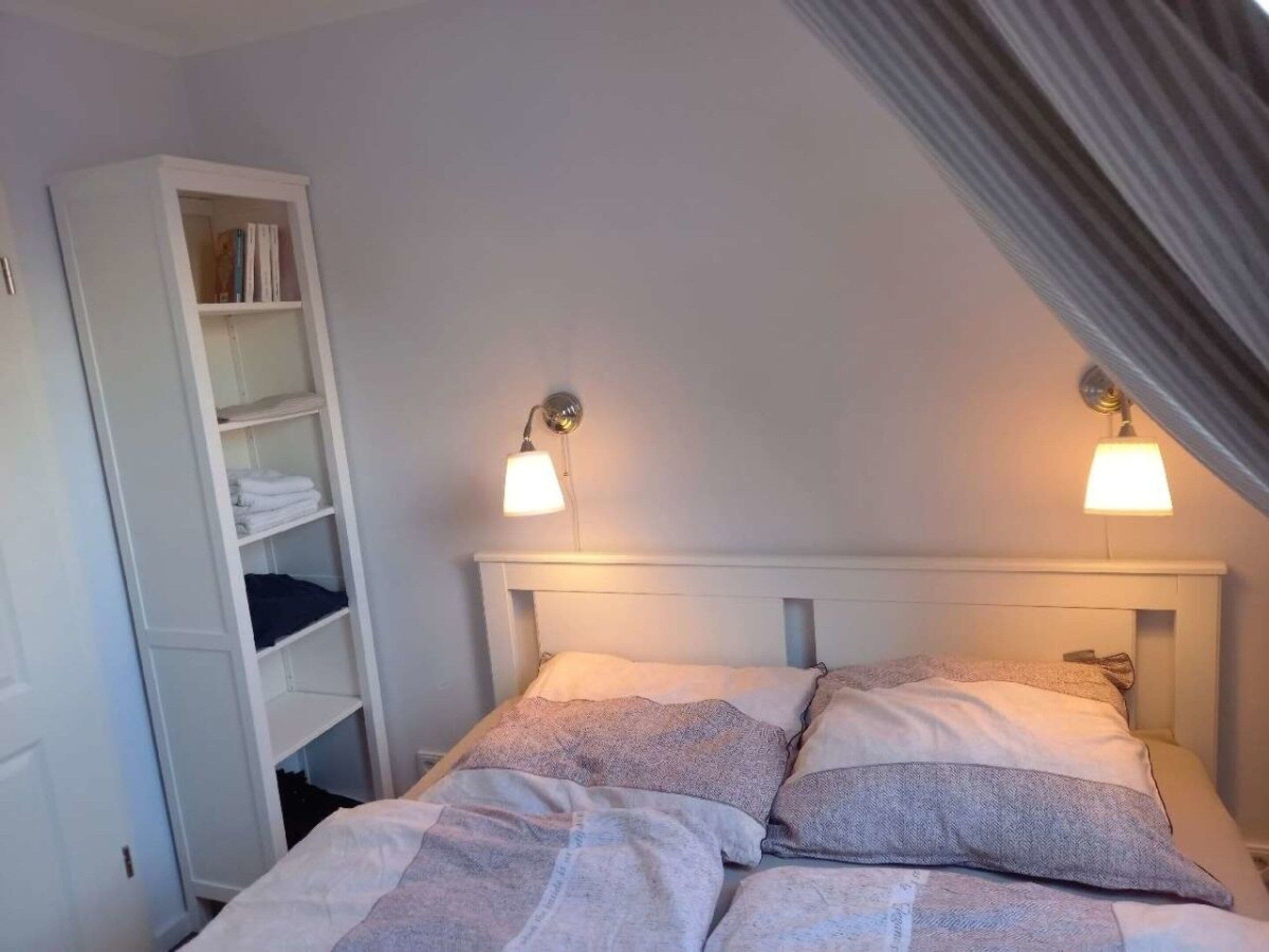 A bedroom with a bed, two bedside lamps, and a white wardrobe.
